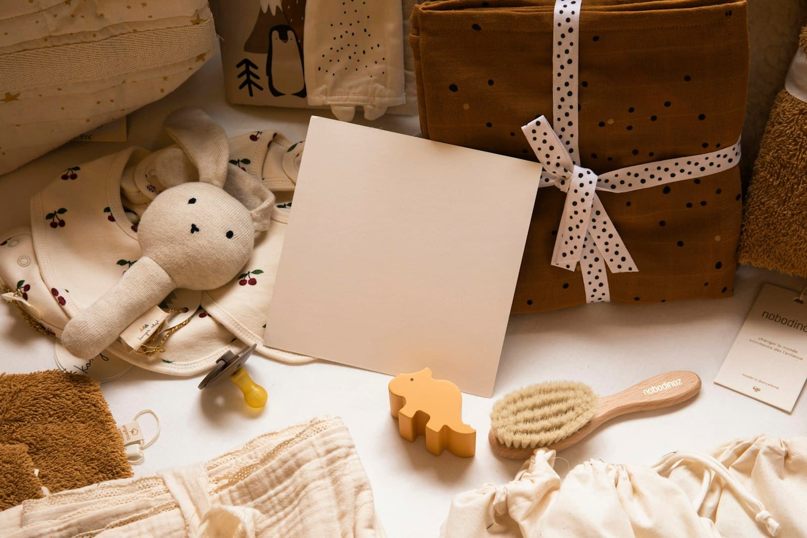 A flat lay of baby gifts — a bunny comforter, a wrapped parcel and a wooden brush